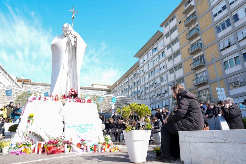Jóvenes y miembros de la Casa de María, grupos asociados a la Pontificia Academia de la Inmaculada Concepción, y otras personas rezan alrededor de una estatua de San Juan Pablo II frente al hospital Gemelli de Roma el 2 de marzo de 2025. El Papa Francisco está recibiendo allí tratamiento para una doble neumonía. (CNS photo/Lola Gomez)