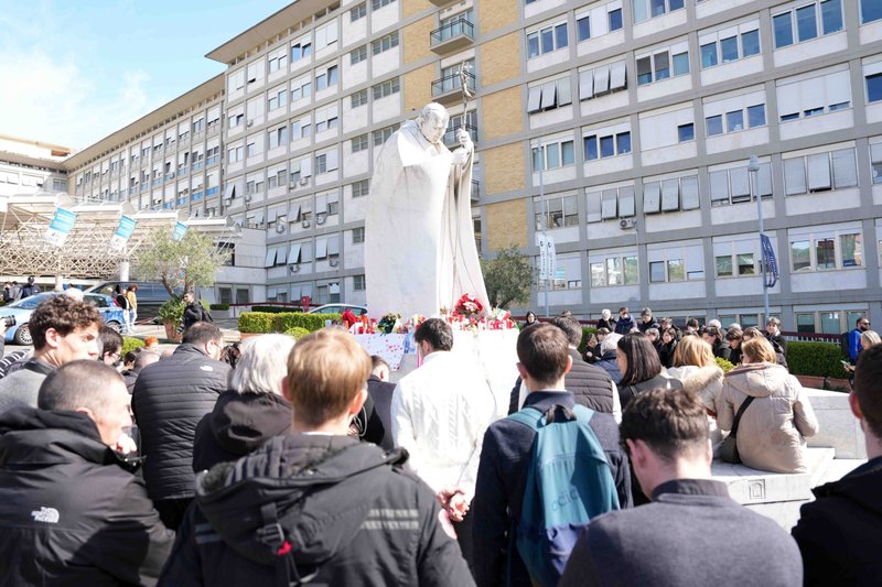 Jóvenes y miembros de la Casa de María, grupos asociados con la Academia Pontificia de la Inmaculada Concepción, y otros fieles rezan alrededor de una estatua de San Juan Pablo II fuera del hospital Gemelli de Roma el 2 de marzo de 2025. El Papa Francisco ha estado hospitalizado desde el 14 de febrero y está recibiendo tratamiento para una doble neumonía. (Foto CNS/Lola Gomez)