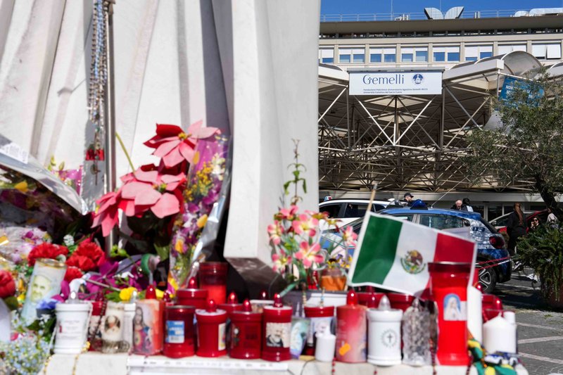 Velas votivas y flores en la base de una estatua de San Juan Pablo II fuera del hospital Gemelli de Roma el 6 de marzo de 2025, donde el Papa Francisco ha estado hospitalizado desde el 14 de febrero, recibiendo tratamiento para una neumonía doble. (CNS photo/Lola Gomez)