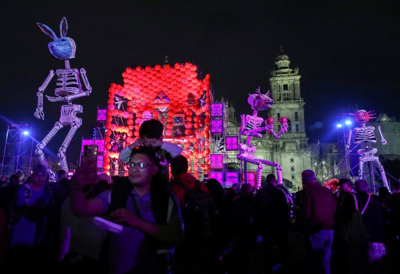 Un hombre se toma una selfie junto a otras personas reunidas cerca de instalaciones artísticas con esqueletos y otras decoraciones en la plaza del Zócalo de Ciudad de México el 30 de octubre de 2024, víspera del Día de Muertos. Al fondo se ve la Catedral Metropolitana. (Foto de OSV News/Henry Romero, Reuters)