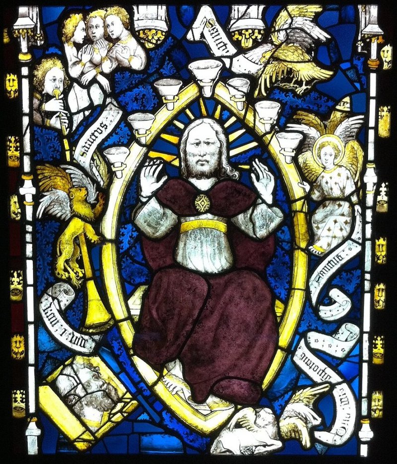 Detalle de “San Juan vislumbra a Dios en la majestad”. Vitral de la ventana este de la catedral de York. San Juan mira a través de una especie de trampilla en la parte inferior izquierda. Dios, en el centro, lo ha convocado al cielo para mostrarle la eternidad. En los pergaminos están escritas palabras de alabanza eterna ofrecidas a Dios por las cuatro criaturas. (Wikimedia Commons)