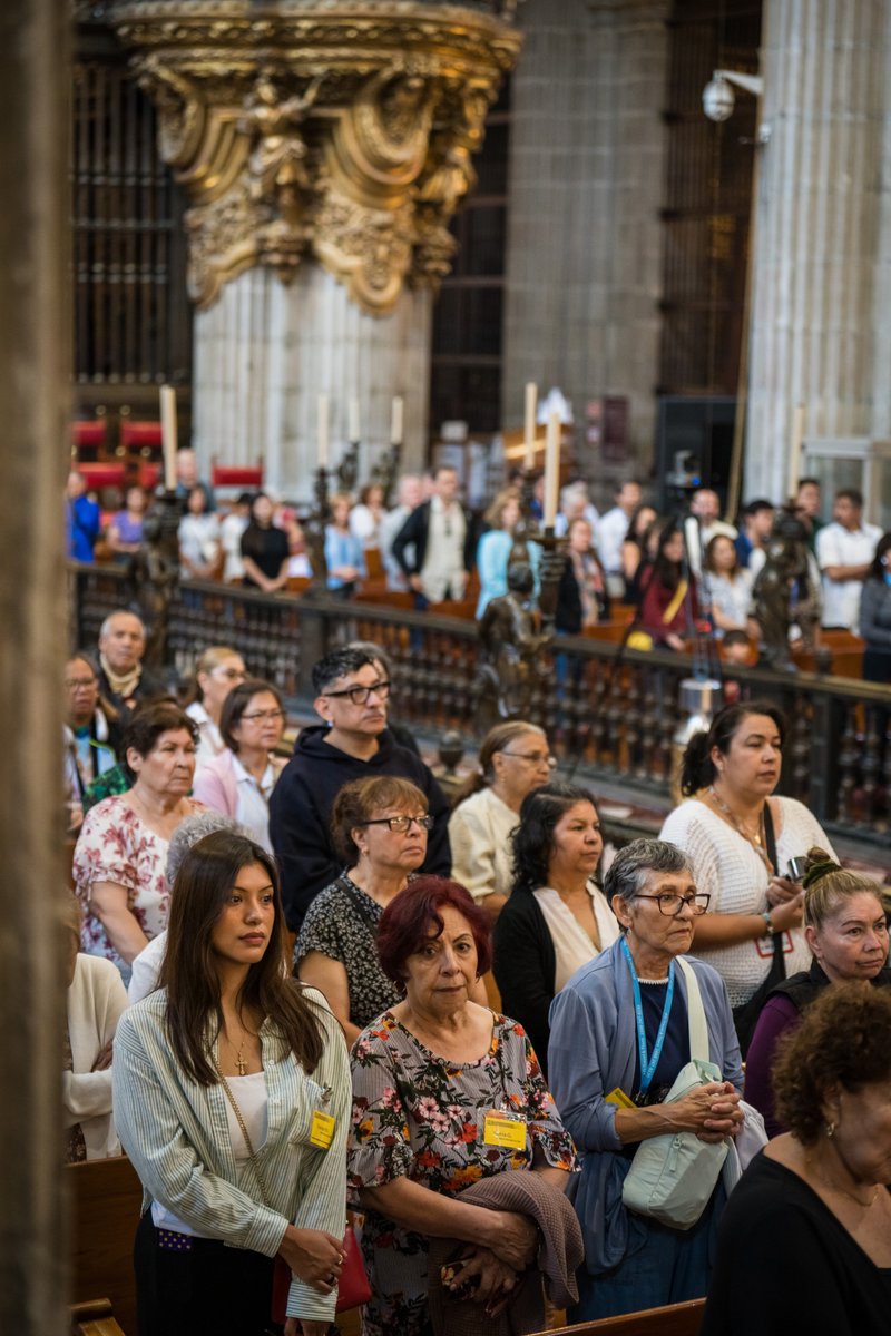 Crowd of worshippers standing in a grand church interior with ornate columns and candles in the background.