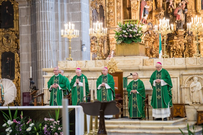 Priests in green liturgical vestments stand at a gold-decorated altar inside a richly ornate church.