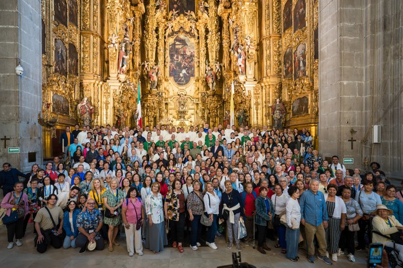 Large group of people posing for a group photo in front of an ornate gilded church altar interior