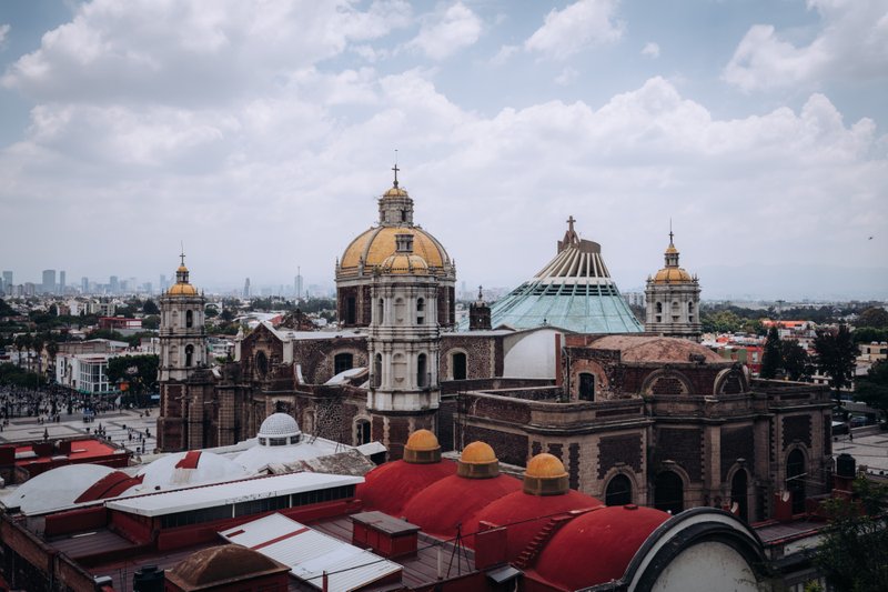 Baroque church towers with gold domes and cross, red brick walls, overlooking a distant city skyline at noon