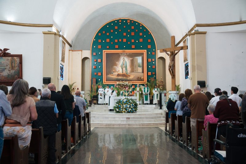 Worshippers stand in pews facing the altar as clergy in green vestments lead a service in a church interior.