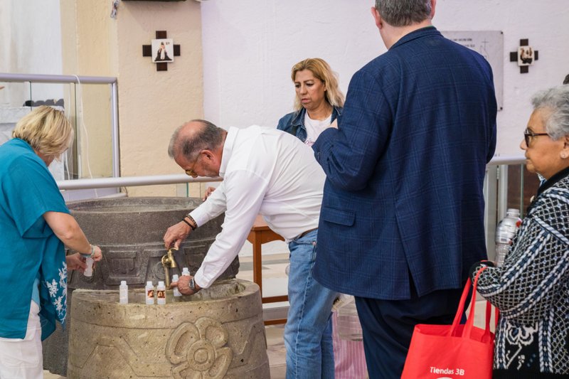 People gather around a stone drinking fountain, filling small bottles from the taps.