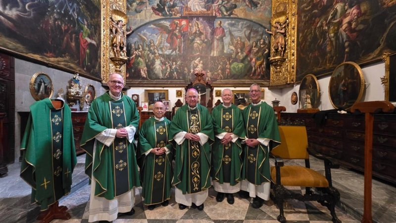 Five priests in green liturgical vestments stand together inside an ornate chapel with golden altarpieces and big mural paintings behind them.