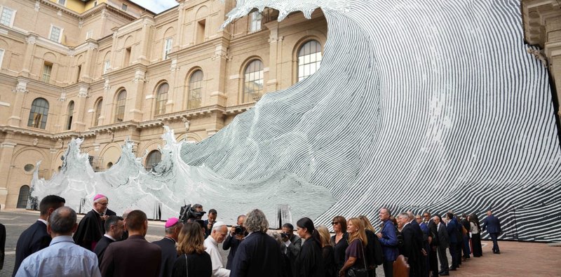 El papa León XIV saluda a los presentes a su llegada para inaugurar la exposición “AQVA. Catástrofe y maravilla” en la Biblioteca Vaticana, el 14 de septiembre de 2026, día de su cumpleaños. La instalación “Wave” o “Diluvium”, del artista francés Jean René, conocido como “JR”, cubre la fachada de la Biblioteca Vaticana. (Foto CNS/Lola Gomez)