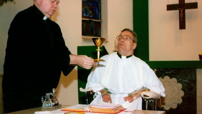 El padre John J. Ferrence, también agustino, eleva el cáliz durante una Misa celebrada por el padre William Atkinson en la escuela secundaria Monsignor Bonner, en Drexel Hill, Pensilvania. Un accidente en trineo dejó al padre Atkinson paralizado de los hombros hacia abajo. (Foto de CNS/Danielle Shields, Catholic Standard and Times)