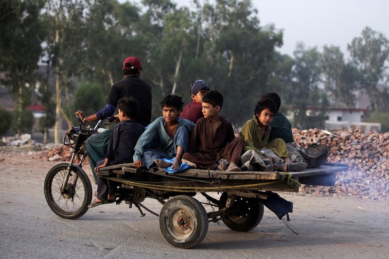 Boys from an Afghan refugee family ride on a motorcycle cart as they head to search for recyclables in Lahore