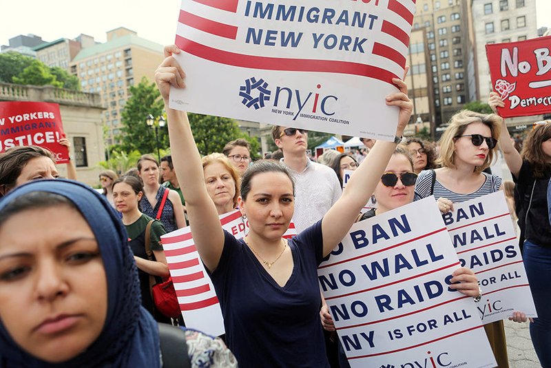 Protesters hold signs against President Donald Trump's limited travel ban that affects refugees and visitors from six Muslim-majority countries in late June in New York City. (CNS photo/Joe Penney