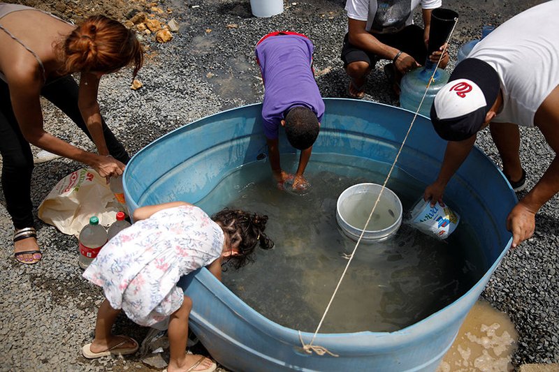 Displaced people fill containers with water Sept. 26 in Canovanas