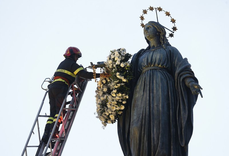 A firefighter places a wreath on a tall statue of Mary overlooking the Spanish Steps in Rome Dec. 8