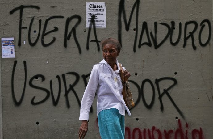 A woman walks past graffiti that says in Spanish: "Get out Maduro. Usurper