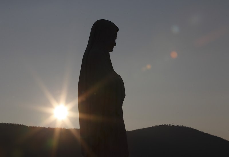 The sun sets behind a statue of Mary on Apparition Hill in Medjugorje