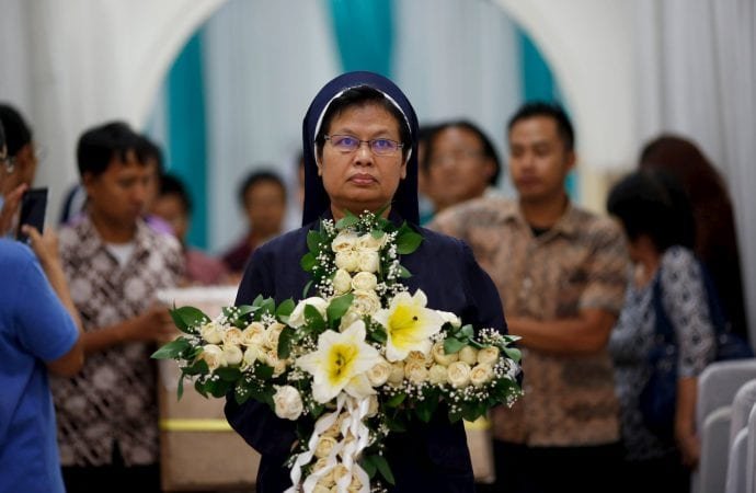 A religious sister carries a cross made of flowers during a funeral in Jakarta