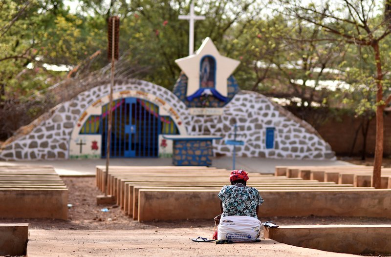 A displaced Christian woman prays in front of a grotto with a statue of Mary in Kaya