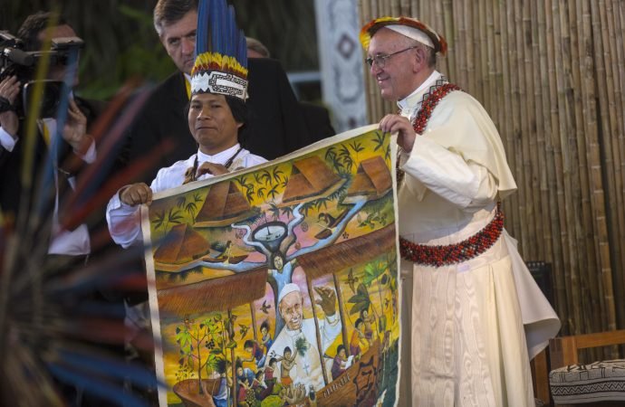 Pope Francis holds one end of a tapestry during a meeting with indigenous groups from the Peruvian Amazon at a coliseum in Puerto Maldonado