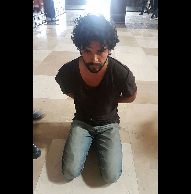 John Rock Schild is seen handcuffed after being accused of stabbing Father Miguel Angel Machorro three times during Mass May 15 at the Metropolitan Cathedral in Mexico City. (CNS photo/EPA)