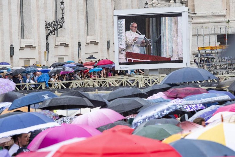 Pilgrims watch Pope Francis on a large screen in the rain as he leads the Angelus Oct. 7 from the window of his studio overlooking St. Peter's Square at the Vatican. (CNS photo/Claudio Peri