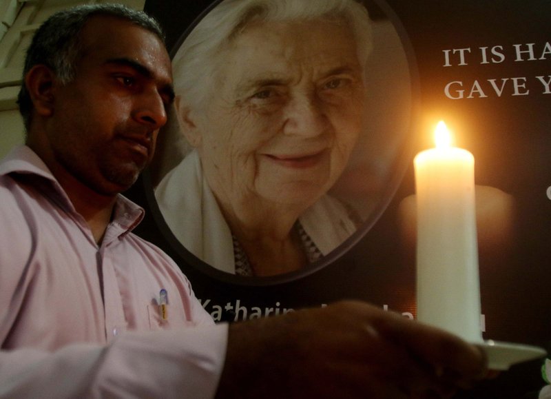 A man holds a candle in front of a portrait of Sister Ruth Katharina Martha Pfau