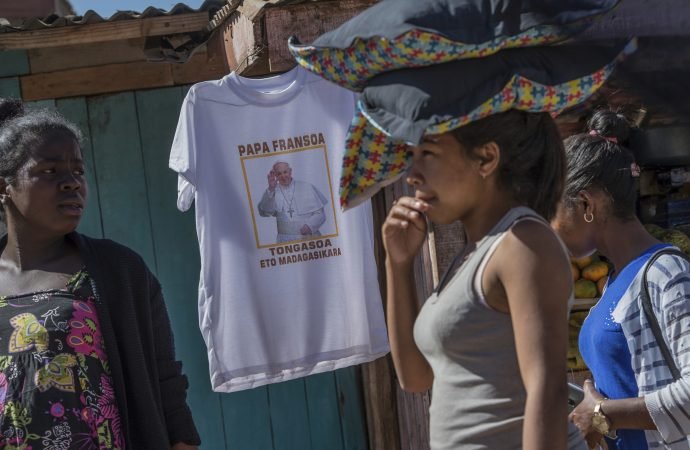 Women carrying bags on their heads pass a stall selling pope t-shirts ahead of the pope's visit to Madagascar next weekend