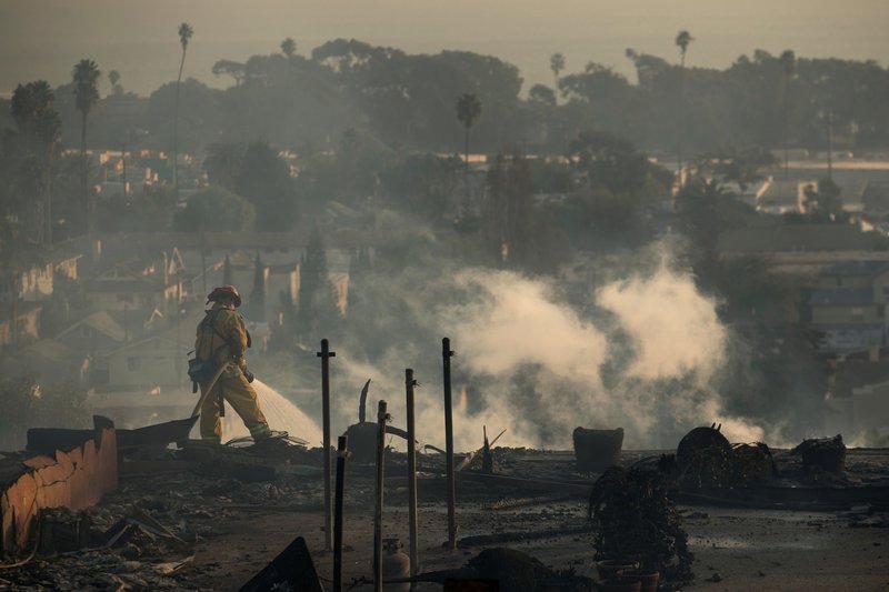 A firefighter sprays water on the remains of the an apartment complex Dec. 5 after a wind-driven wildfire swept into Ventura