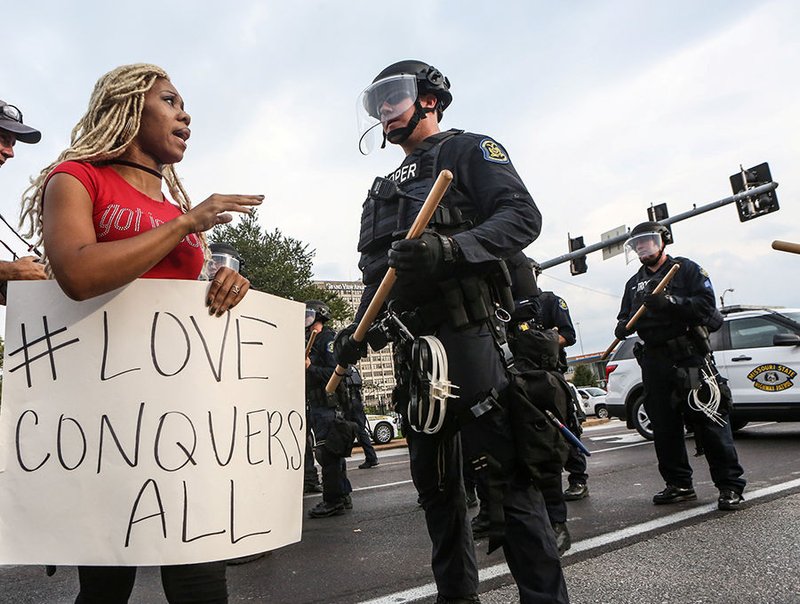 A woman says a prayer next to a police officer in riot gear during Sept. 17 protests after a not-guilty verdict in the murder trial of former St. Louis police officer Jason Stockley