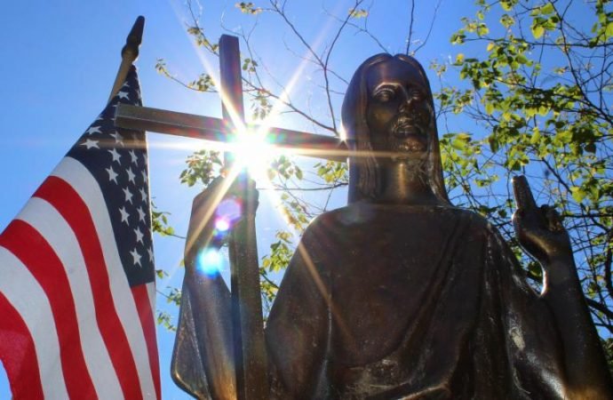 Sun shines through a statue of Christ on a grave marker alongside an American flag June 7 at St. Mary Catholic Cemetery in Appleton