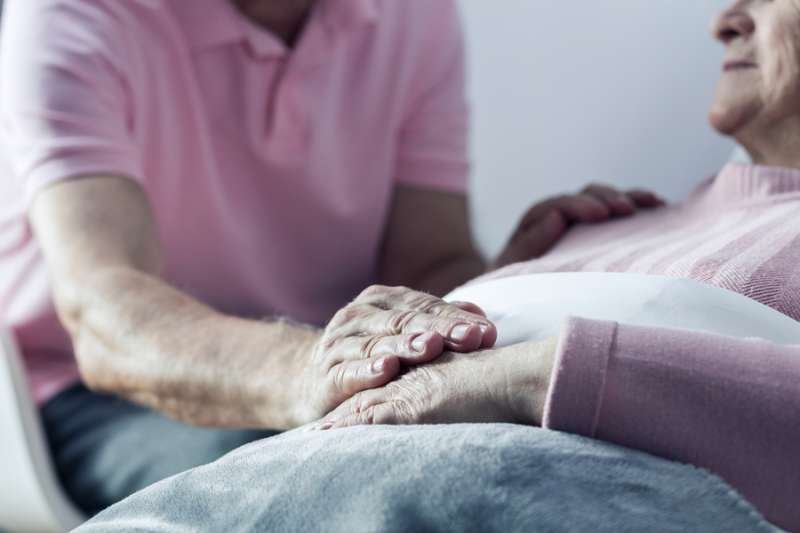 Senior man holding hand of his ill wife. Credit: Shutterstock