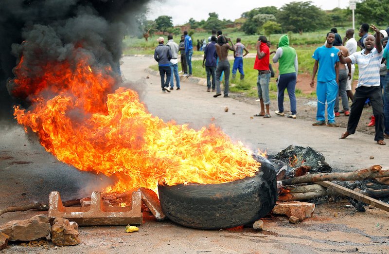 Protesters stand behind a burning barricade during protests over steep fuel price hikes Jan. 15 in Harare