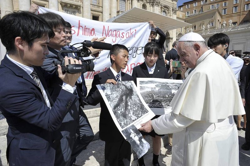 Pope Francis examines photos of the aftermath of the 1945 atomic bombing of Japan as he greets members of the Hiroshima and Nagasaki Youth Peace Messengers at his weekly general audience June 19
