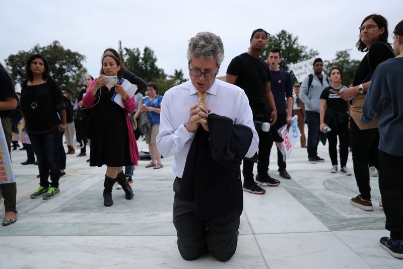 A man prays amid protesters demonstrating on the steps of the U.S. Supreme Court building in Washington Oct. 6 as Judge Brett Kavanaugh is sworn in as an associate justice inside. (CNS PHOTO/JONATHAN ERNST