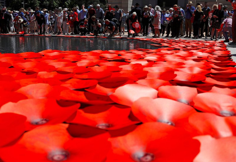 Members of the public place floating poppies onto a pond during a memorial service at the ANZAC War Memorial to mark the centenary of the armistice ending World War I