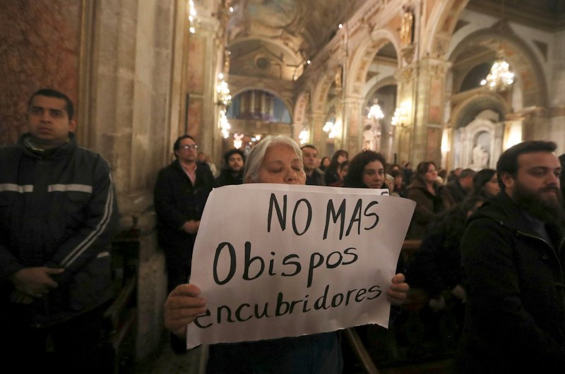 A woman holds a sign in protest while praying as Cardinal Ricardo Ezzati of Santiago