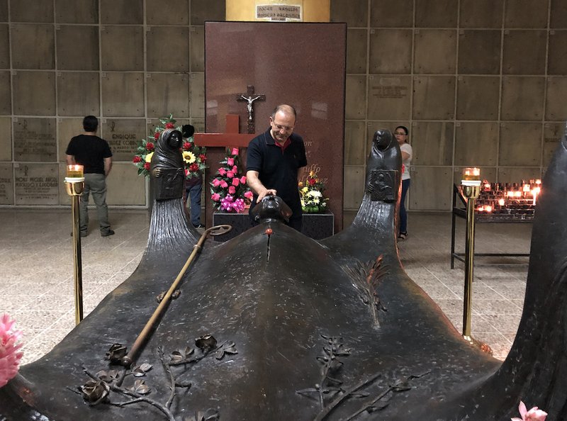 Italian pilgrim Thierry Bonaventura touches a sculpture that covers the burial place of St. Oscar Romero at the crypt in the Metropolitan Cathedral of San Salvador