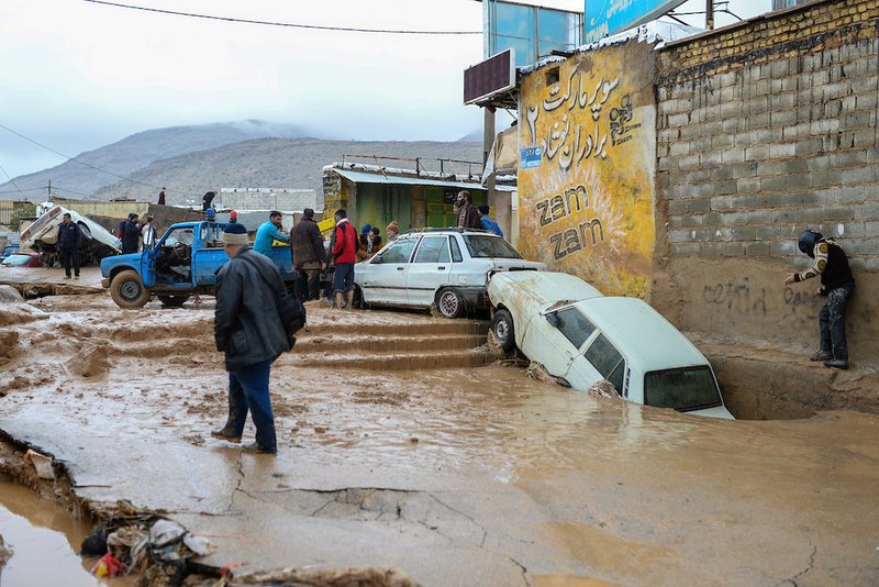 People walk near damaged vehicles after flooding in Shiraz