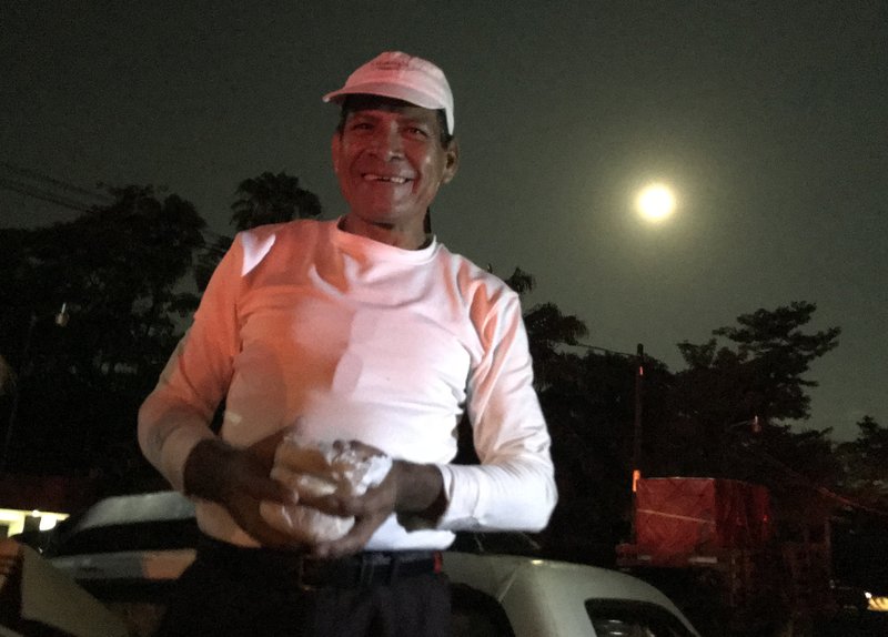 Rafael Gomez offers sandwiches to migrants moving north in a caravan in the early morning hours of Oct. 24 as they leave Huixtla