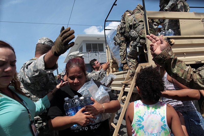 A woman carries bottles of water and food during a distribution of relief items Sept. 24 in San Juan