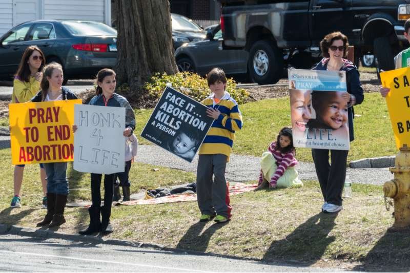 Adult and young people hold signs protesting abortion. Credit: Murloc / Shutterstock
