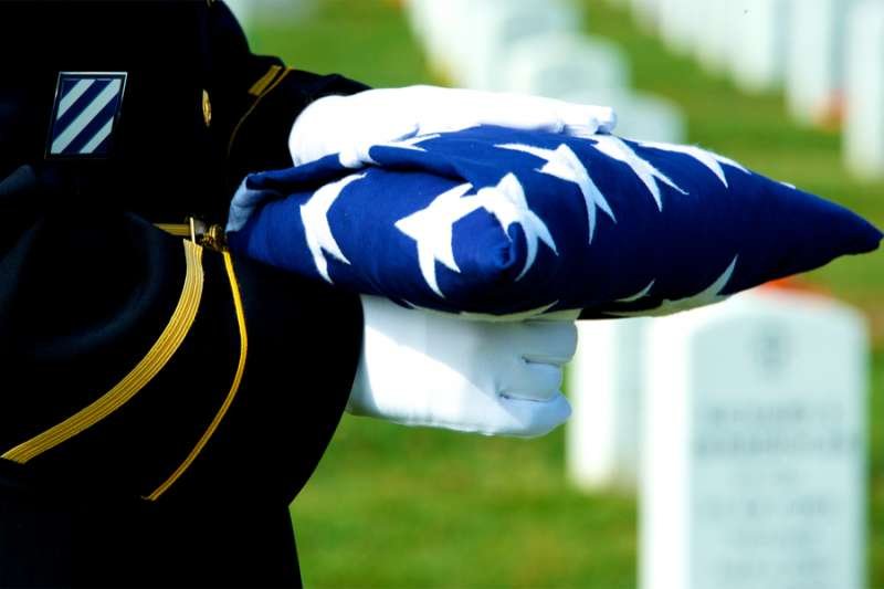 Honor Guard holding folded American flag at grave site at Arlington National Cemetery. Stock photo via Shutterstock