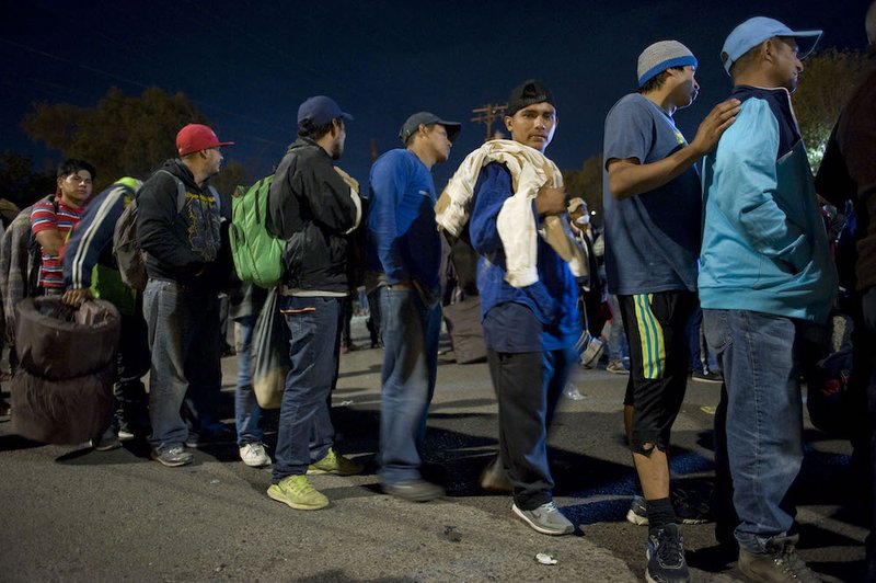 People wait in line in the evening to enter a camp at a sports facility in Tijuana
