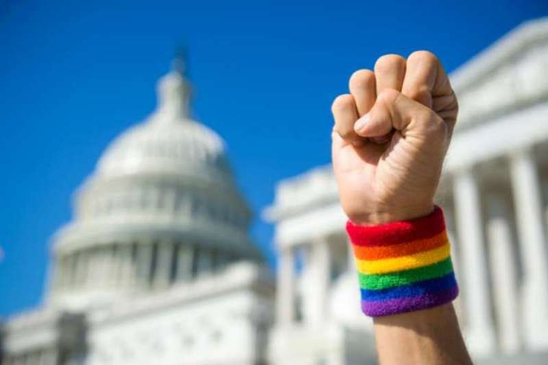 Hand wearing gay pride rainbow wristband making a power fist gesture in front of the US Capitol Building in Washington