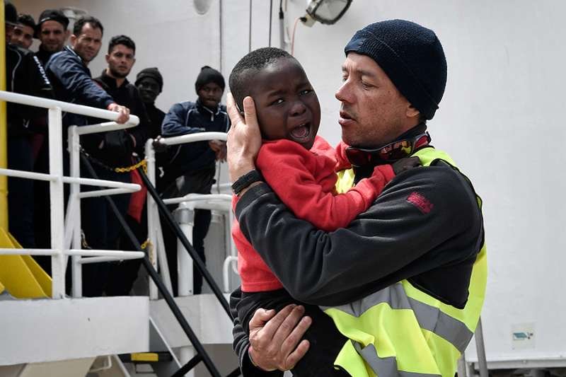A helper from Doctors Without Borders holds a Nigerian child as the MV Aquarius arrives at the Sicilian port of Messina