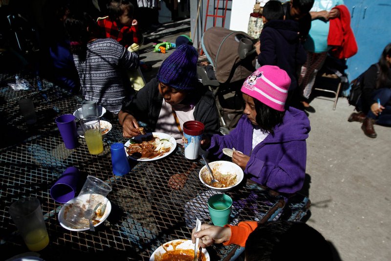 Central American migrants eat a meal while waiting for their asylum requests to be processed at a shelter in Tijuana