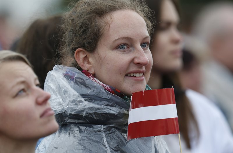 A young woman holds the Latvian flag as Pope Francis celebrates Mass Sept. 24 at the Shrine of the Mother of God in Aglona