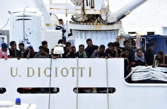 Migrants aboard the Italian Coast Guard ship Diciotti gather on the deck as they await decisions in the port of Catania