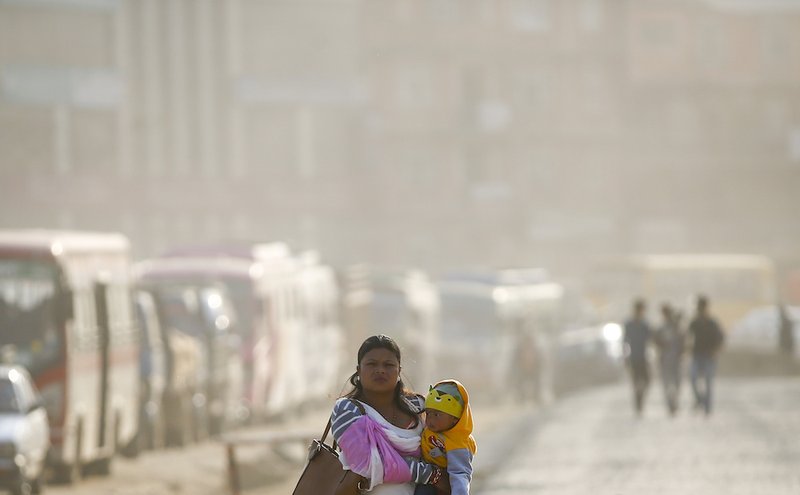 A woman carries a child through air pollution in Kathmandu