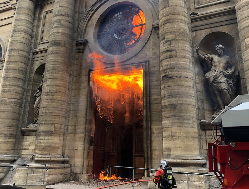 A firefighter is seen as flames shoot through the front door of St. Sulpice Church in Paris March 17